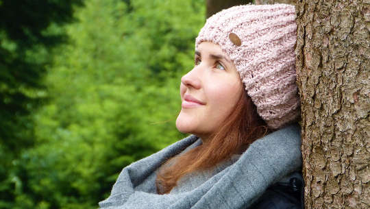 The Greedy Reason for Being Optimistic and Having Gratitude smiling woman resting against a tree trunk